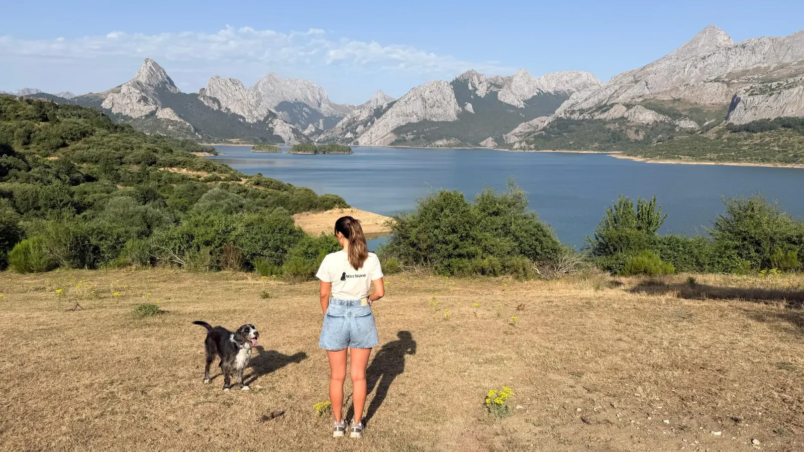 Kelly, de espaldas, junto a su perro frente a un embalse azul rodeado de montañas de roca